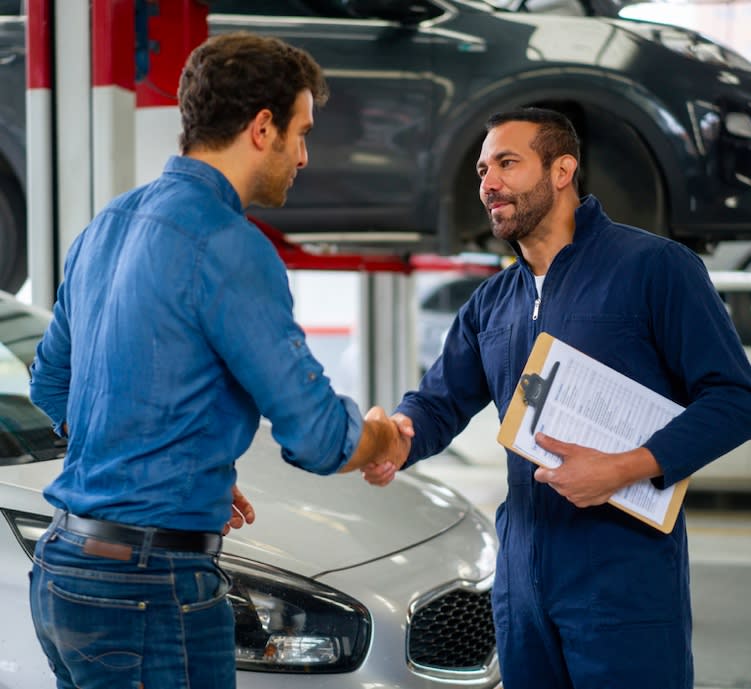Car maintenance specialist in a workshop shaking hads with a client