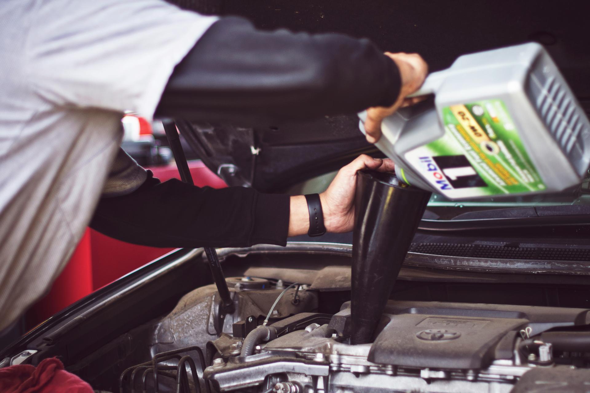 red car, hood open, hands of man changing car oil