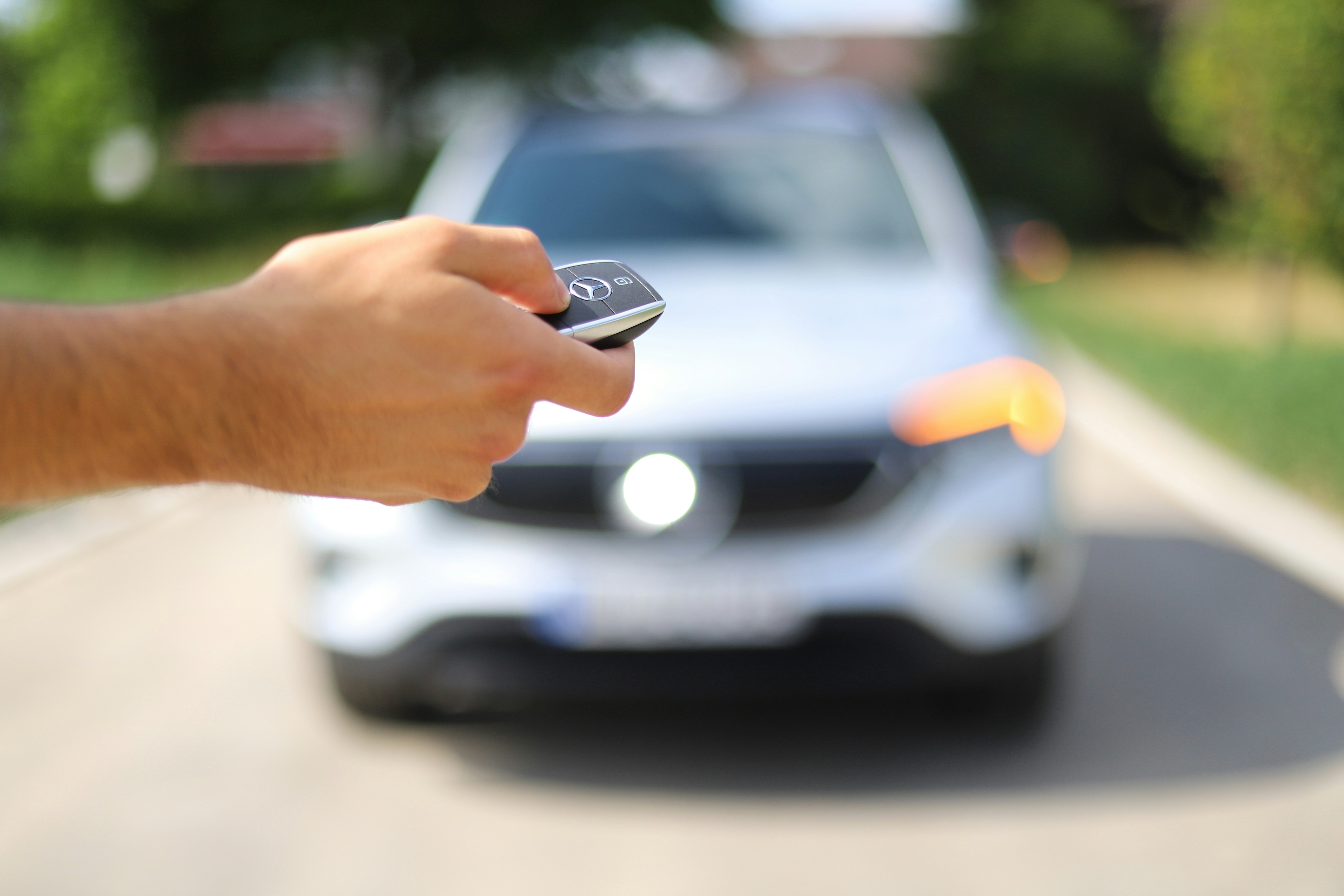 Man's hand holding remote car key for Mercedes with out of focus silver SUV in background